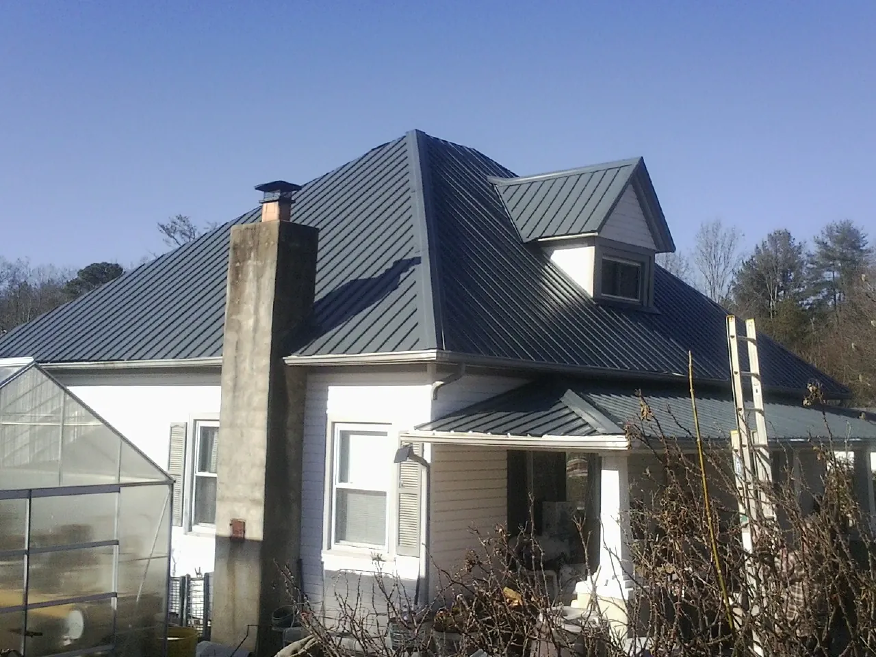 Dark blue standing seam metal roof on a white farmhouse with dormer — Slate & Tile Roof Repair by Roofing Brothers in Sutersville
