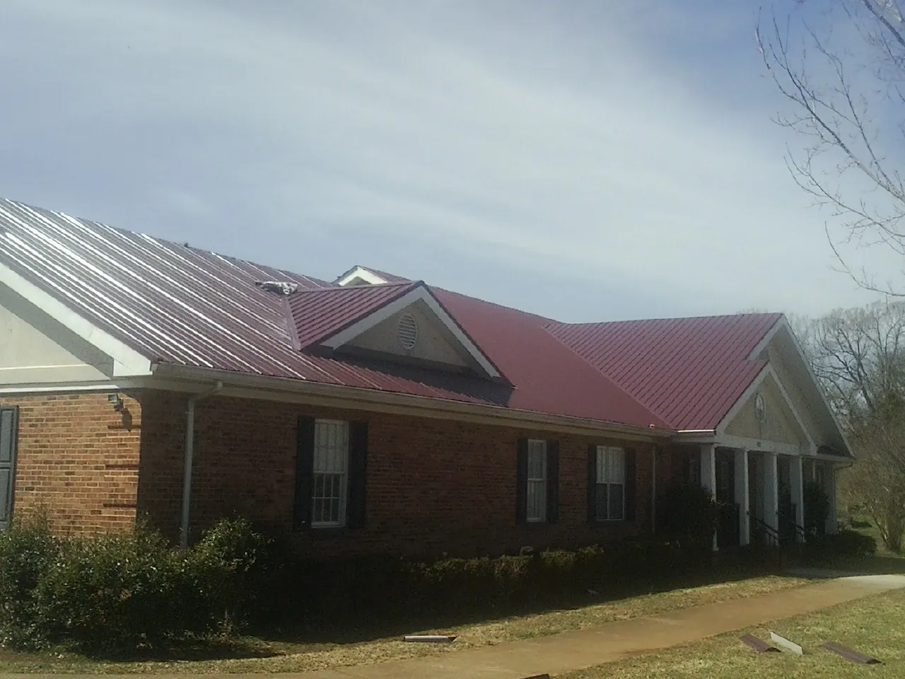 Red metal roof with gabled entries on a long brick building, from a Hail Damage Roof Repair job in Sutersville