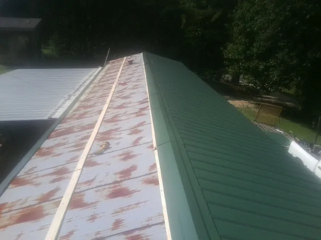 Old rusted panels beside newly installed green metal roofing — Wind Damage Roof Repair by Roofing Brothers in Sutersville