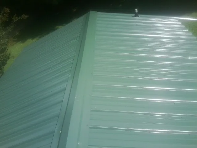 New green metal panels meeting at the ridge of a roof — Flat Roof Repair work by our crew in Sutersville