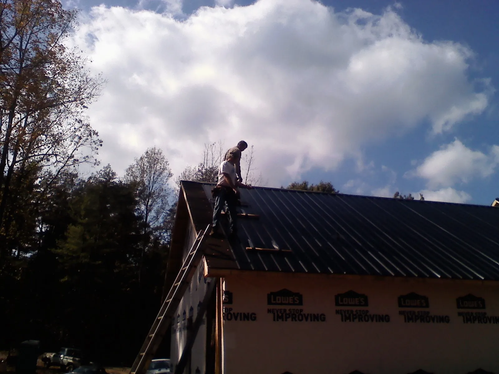 Roofer fastening dark metal panels high against a cloudy sky, from a Roof Inspection job in Sutersville
