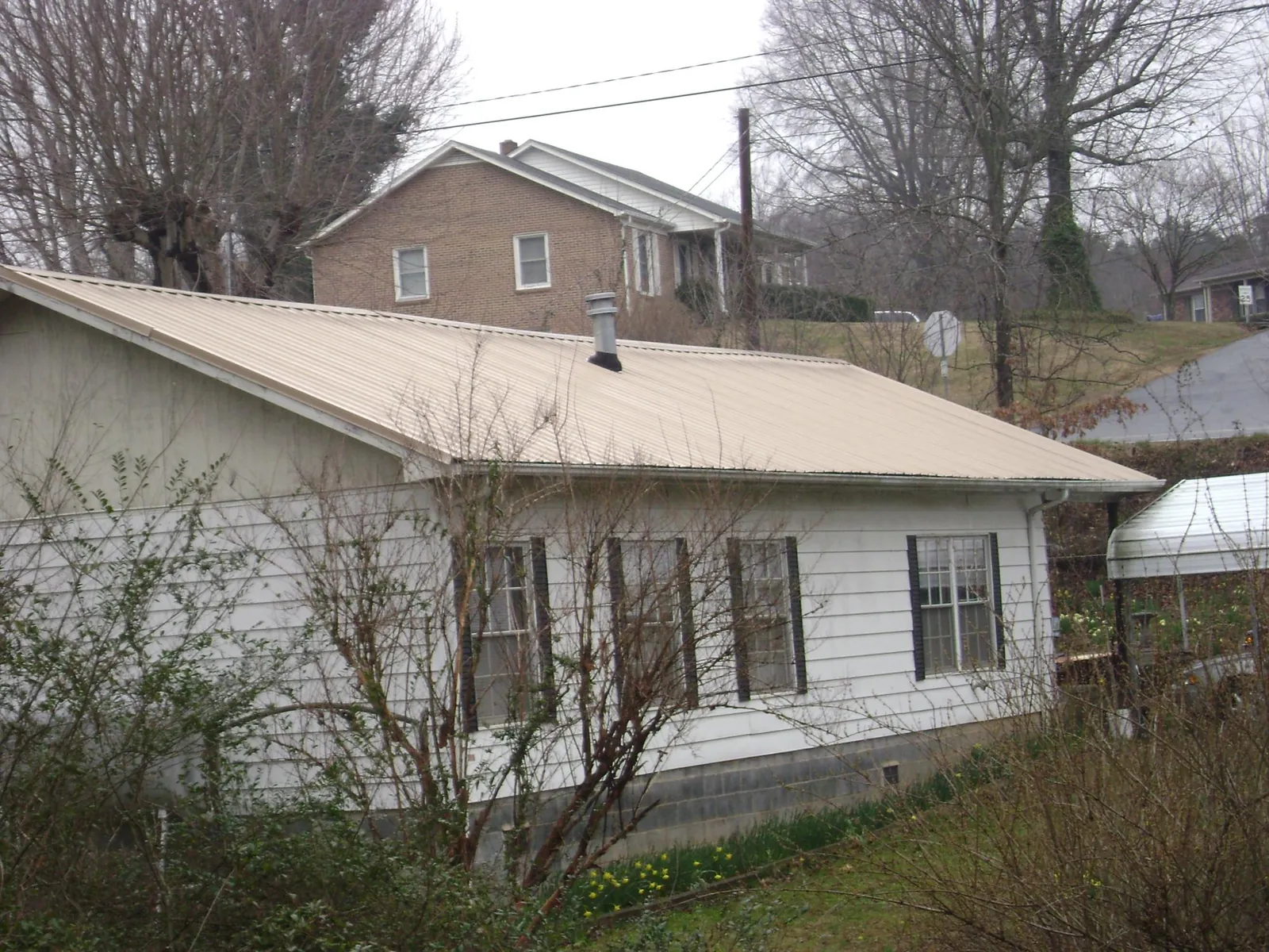 Tan metal roof on a white sided house set into a hillside — Commercial Roofing by Roofing Brothers in Sutersville